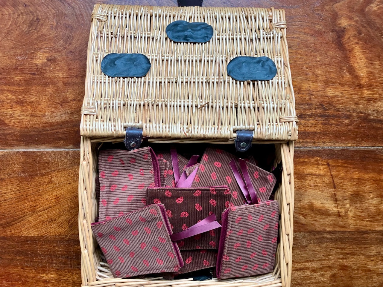 Wicker basket with Brown and Rose Paisley Needle Cases inside on a wooden table.