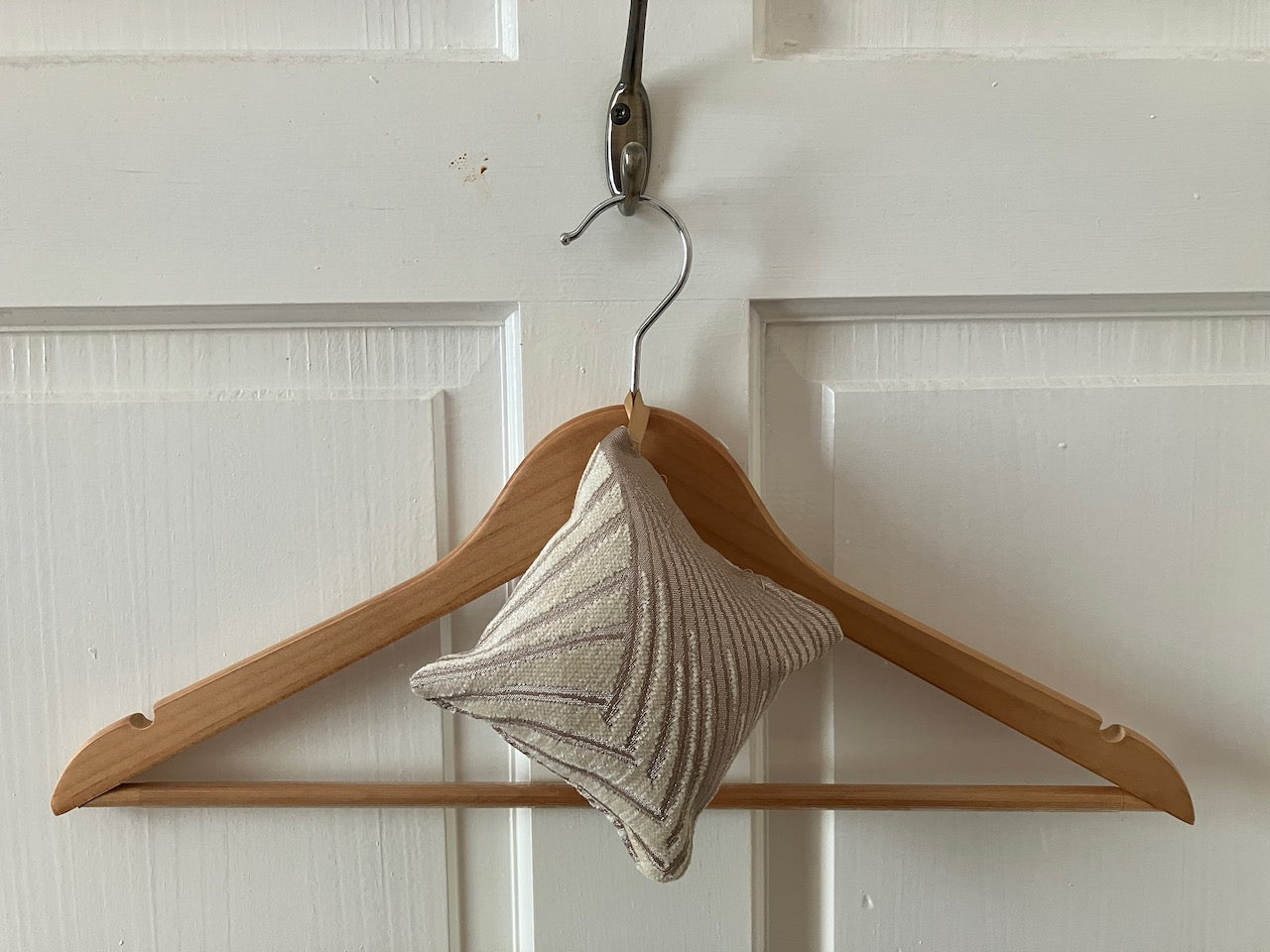 Wooden hanger with an Art Deco Scented Cushion against a white paneled door