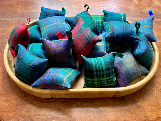 Various coloured Tartan Pin-Cushions on a wooden tray on a wooden table.