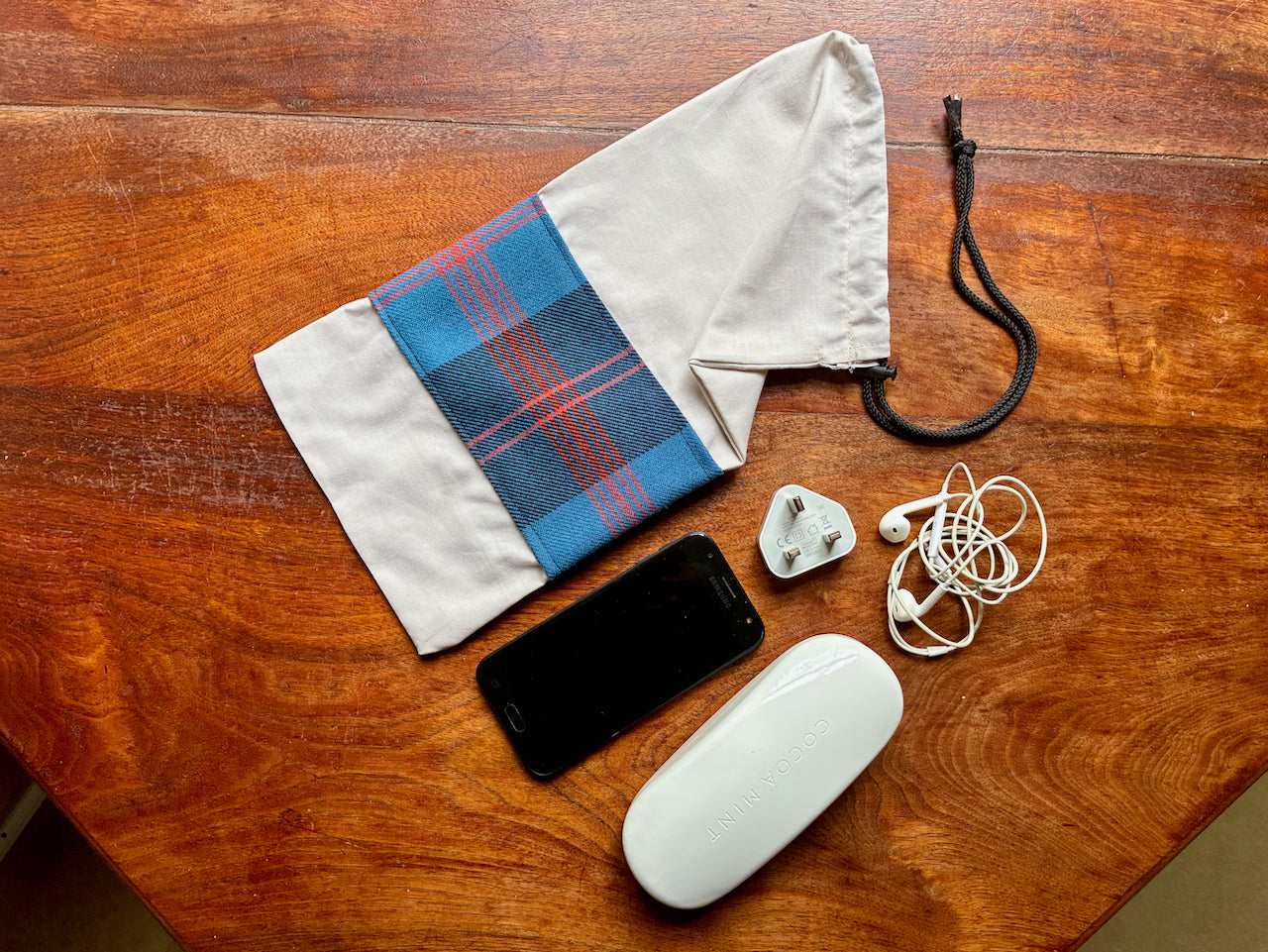 Phone, plug, spectacle case, ear-buds beside  a Tartan Drawstring Bag by Curlew Crafts