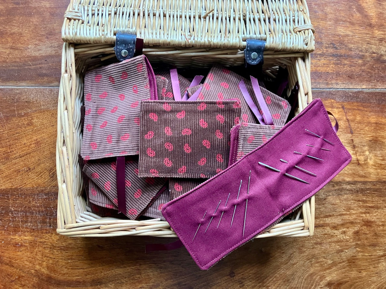 Basket with Brown and Rose Paisley Needle Cases inside on a wooden table.